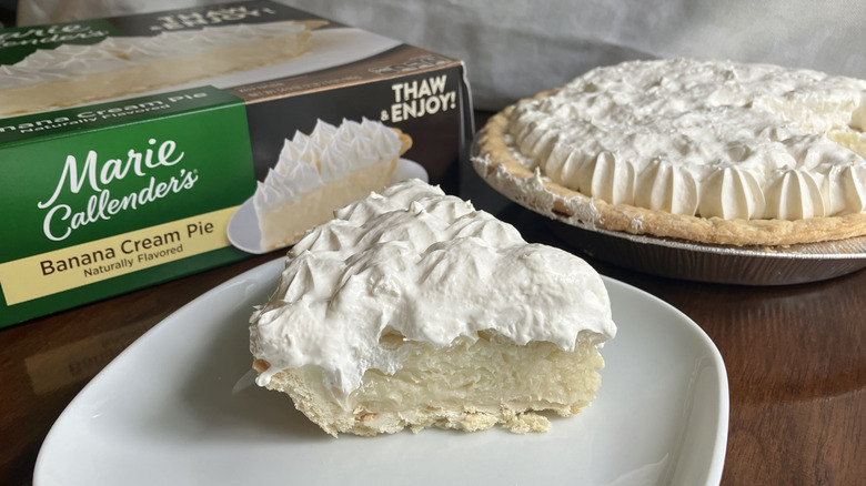 A slice of Marie Callender's Banana Cream Pie next to its box and the rest of the pie in its tin