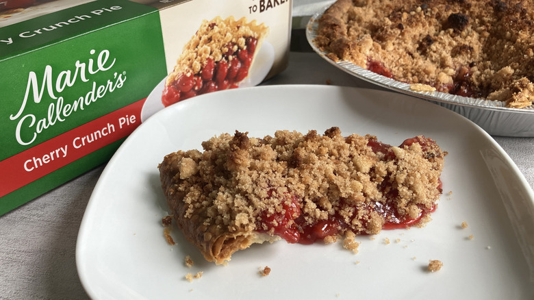 A slice of Marie Callender's Cherry Crunch Pie next to its box and the rest of the pie in its tin