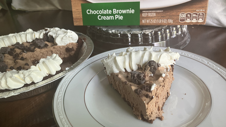 A slice of Marie Callender's Chocolate Brownie Cream Pie next to its box and the rest of the pie in its tin