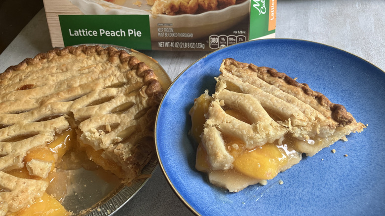 A slice of Marie Callender's Lattice Peach Pie on a blue plate sits atop the pie it was sliced from