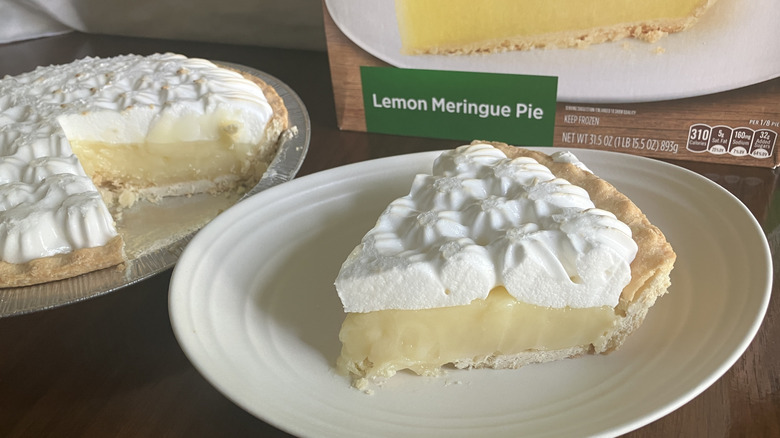 A slice of Marie Callender's Lemon Meringue Pie next to its box and the rest of the pie in its tin