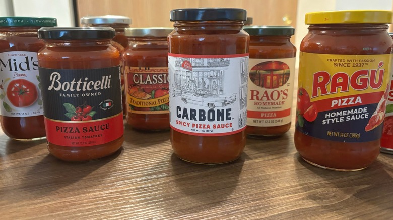 Several brands of store bought pizza sauce jars on a wooden table