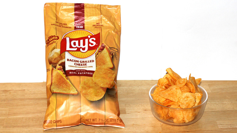 A bag of Lay's Bacon Grilled Cheese potato chips beside a bowl full of chips