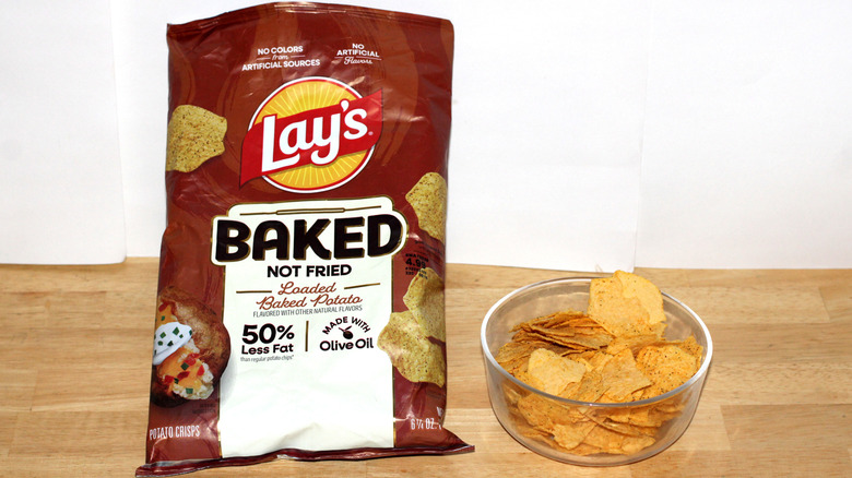 A bag of Lay's Baked Loaded Potato potato chips beside a bowl full of chips