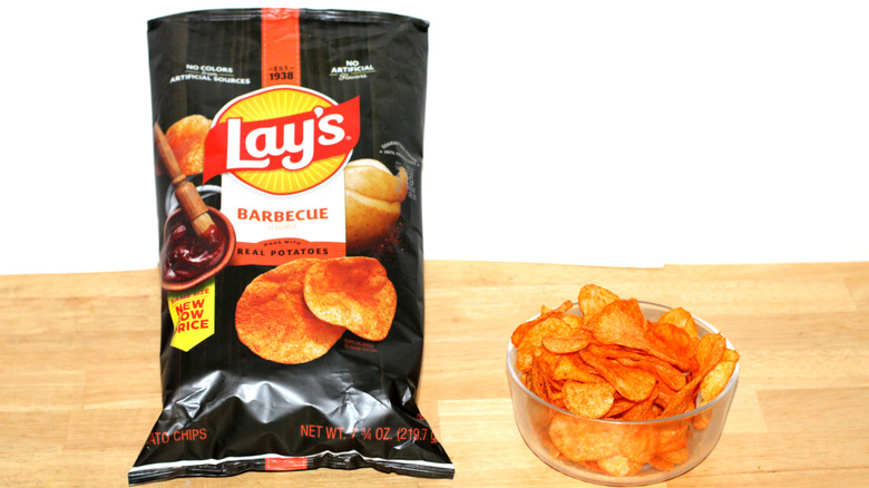 A bag of Lay's  Barbecue potato chips beside a bowl full of chips