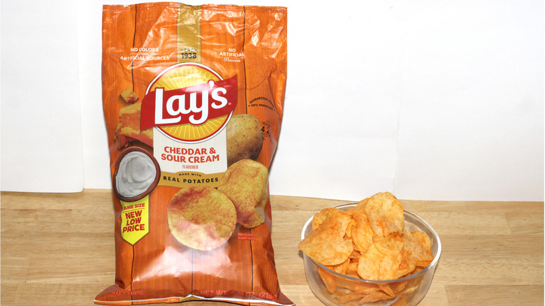 A bag of Lay's Cheddar & Sour Cream potato chips beside a bowl full of chips