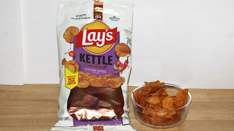 A bag of Lay's Kettle Cooked Cajun Spice potato chips beside a bowl full of chips