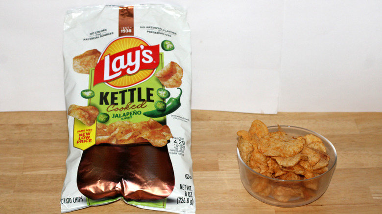 A bag of Lay's Kettle Cooked Jalapeño potato chips beside a bowl full of chips
