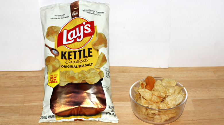 A bag of Lay's Kettle Cooked Original potato chips beside a bowl full of chips