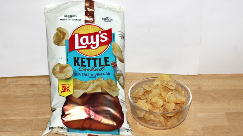 A bag of Lay's Kettle Cooked Salt & Vinegar potato chips beside a bowl full of chips