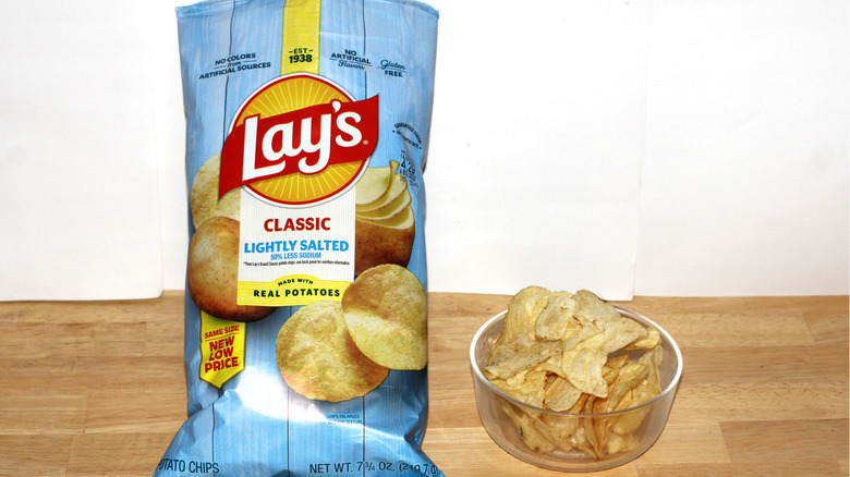 A bag of Lay's Lightly Salted potato chips beside a bowl full of chips
