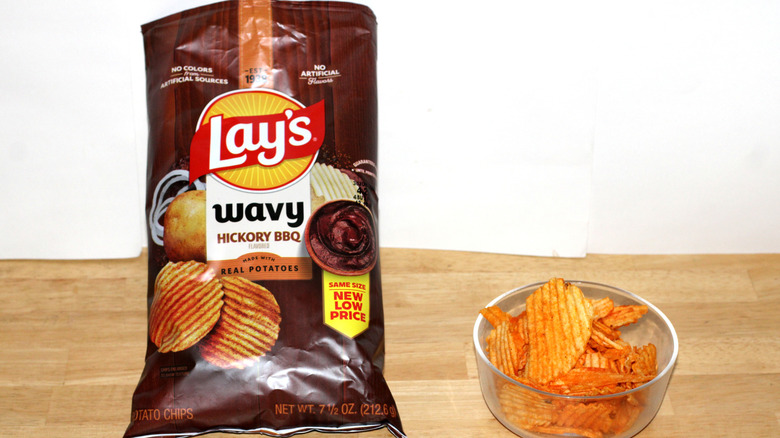 A bag of Lay's Wavy Hickory BBQ potato chips beside a bowl full of chips