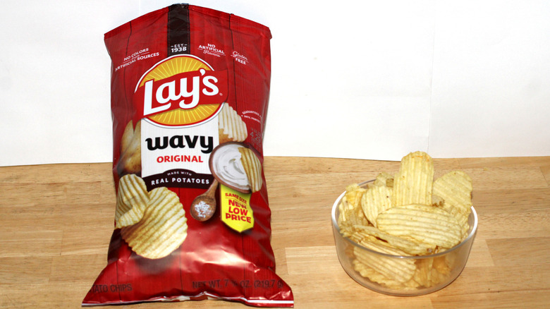A bag of Lay's Wavy Original potato chips beside a bowl full of chips