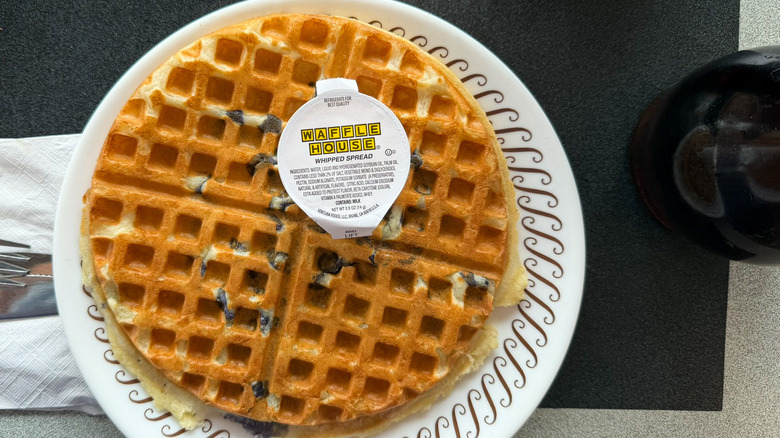 A blueberry nougat waffle on a Waffle House table on a white plate with a package of whipped spread on top