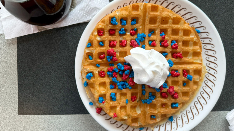 A firework waffle on a Waffle House table served on a white plate topped with a dollop of whipped cream