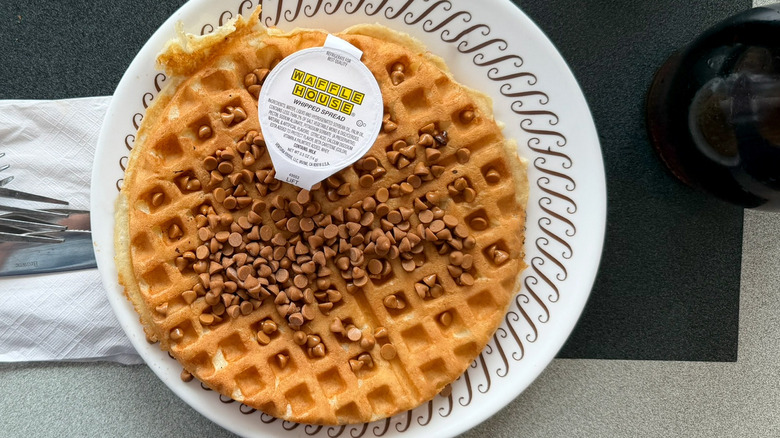 A peanut butter chip waffle on a Waffle House table on a white plate with a package of whipped spread on top