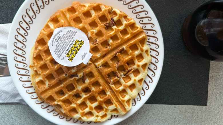 A pecan waffle on a waffle house table on a white plate topped with a package of whipped spread