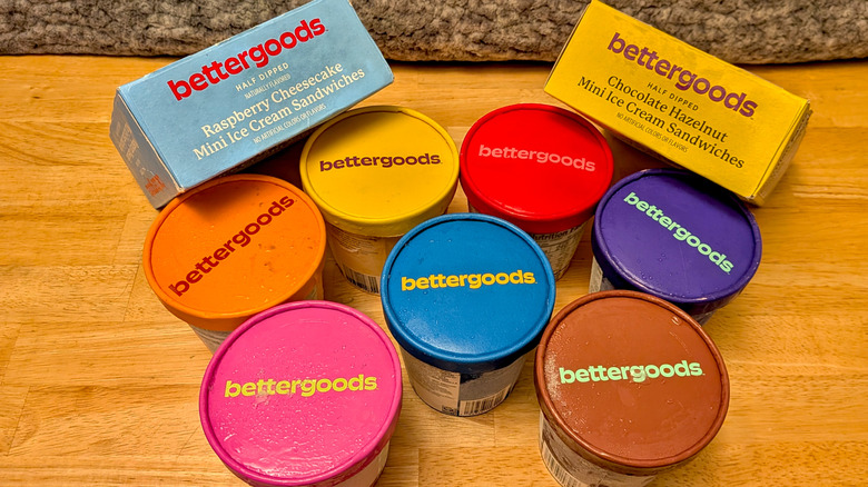 A selection of 9 different Bettergoods branded ice cream based desserts including pints of ice cream and two boxes of ice cream sandwiches viewed from above with most of the labels hidden and all logos facing upwards