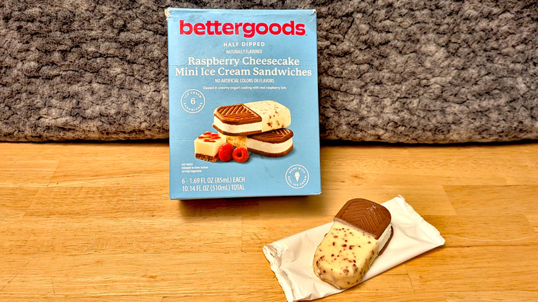 A box of Walmart's Bettergoods brand Raspberry Cheesecake Mini Ice Cream Sandwiches beside an unwrapped ice cream sandwich