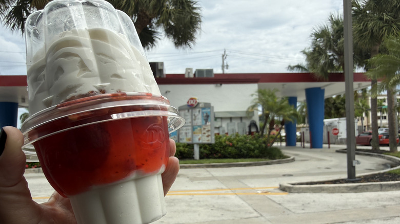 Hand holding Dairy Queen strawberry sundae out car window in Dairy Queen parking lot