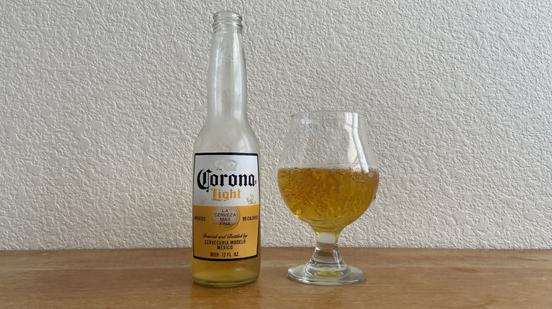 Corona Light bottle beside tulip glass half-full of beer