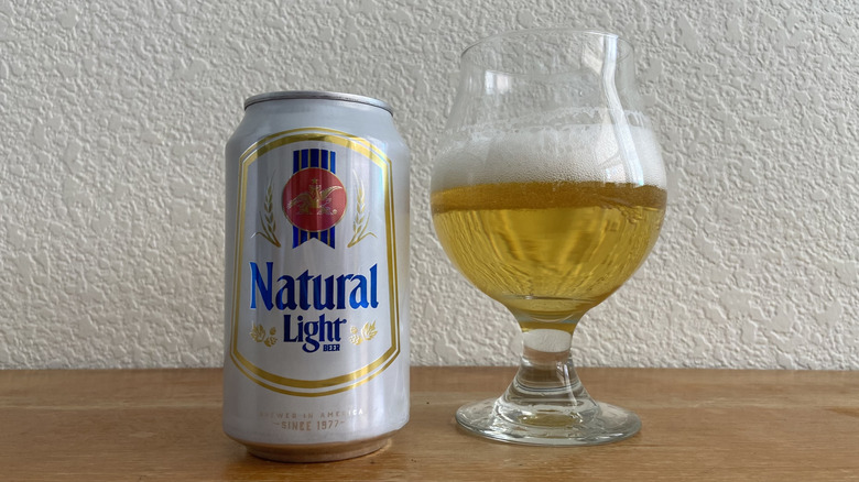 Natural Light can beside tulip glass half-full of beer