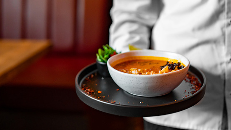 Close-up of a bowl of soup on a tray being served by a chef