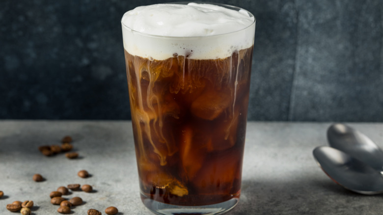 A glass cup of cold brew coffee with foam on top.