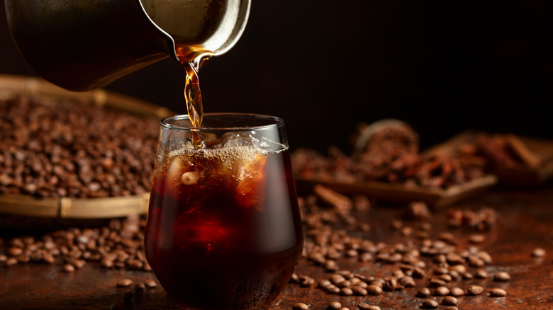Black iced coffee being poured into a glass.