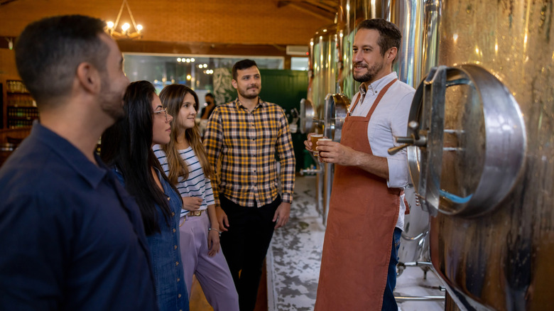 A worker at a brewery taking customers on a tour of the establishment.