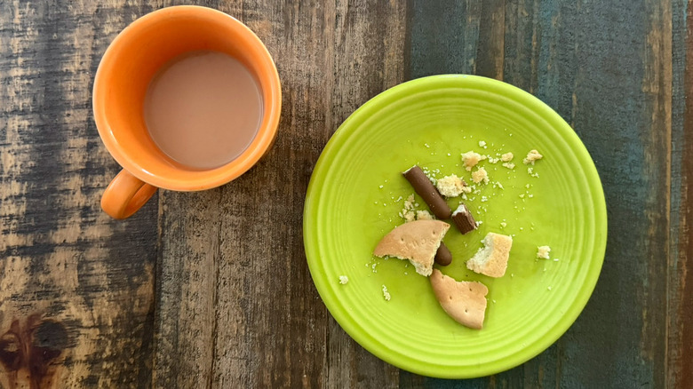 A half-drunk mug of tea next to a plate with biscuit crumbs