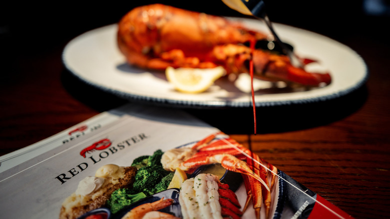 A Red Lobster menu on a table with a plate with a whole lobster and lemon slices in the background