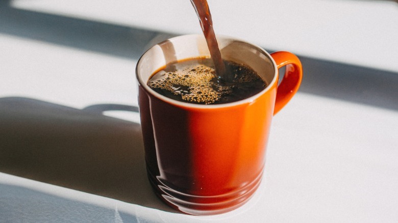 Coffee being poured into an orange mug.