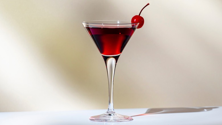 A Manhattan cocktail in a glass with a cherry on the side
