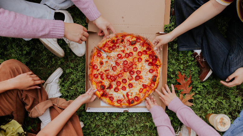 A group of friends each grab a slice of New York-style pizza while sitting in Central Park.