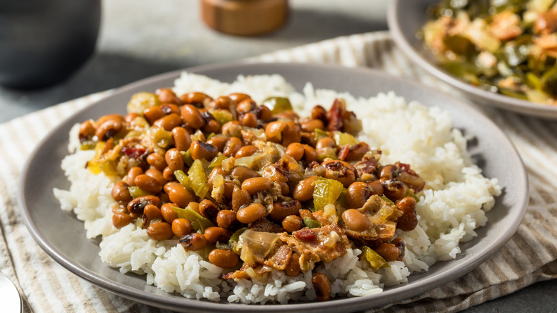 A plate of Hoppin' John over white rice, which includes peas, vegetables, and pork