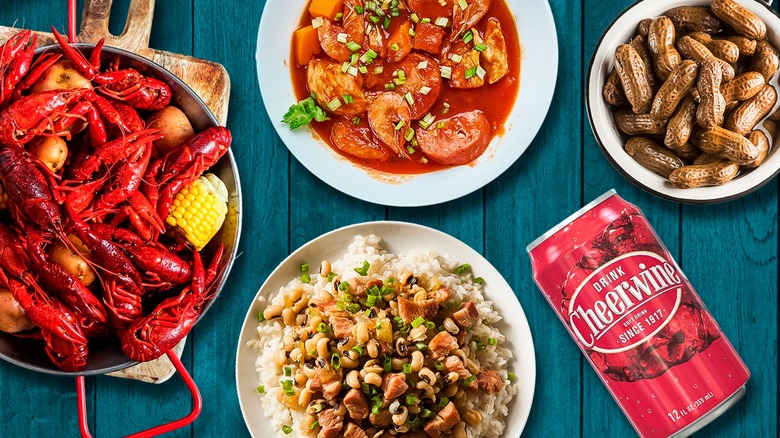 Montage image of several popular Southern foods, like peanuts, gumbo, a red can of cheerwine, and crawfish, all on blue picnic table background