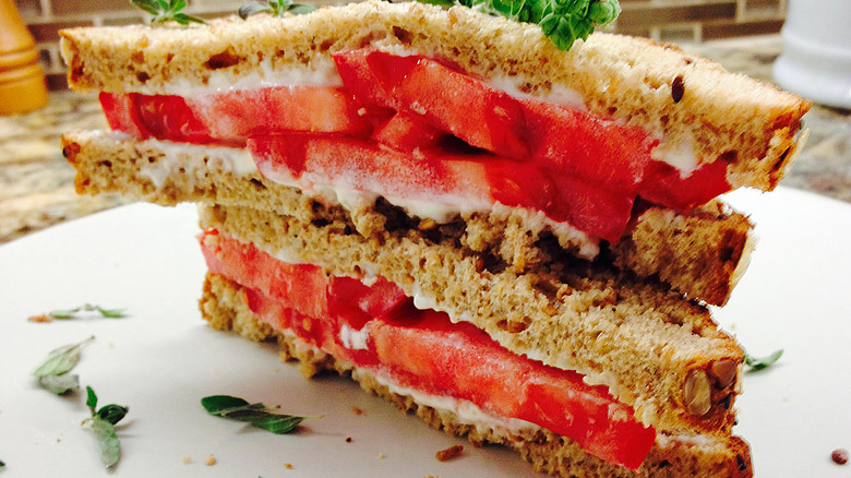 Stacked tomato sandwich halves with whole wheat bread and thick red tomato slices on white plate