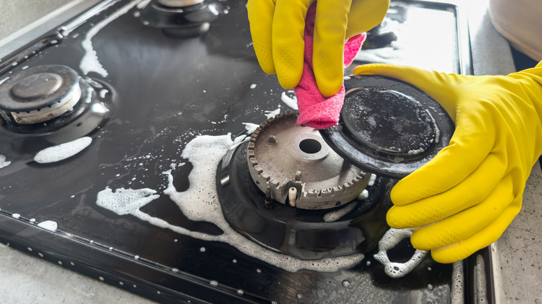 Cleaning a gas stove with gloves and a soapy solution