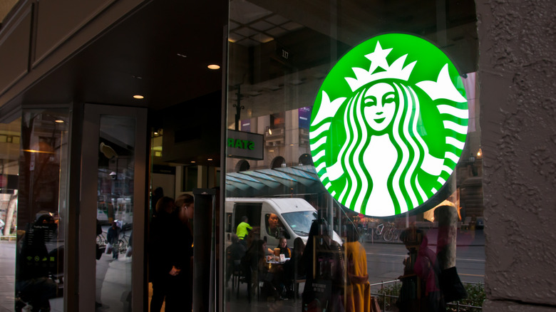 The Starbucks sign in the window of a Starbucks location in a city