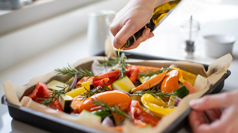 Drizzling oil on a tray of chopped vegetables and herbs