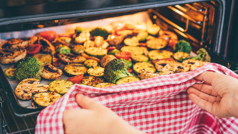 Removing a tray of roasted vegetables from an oven