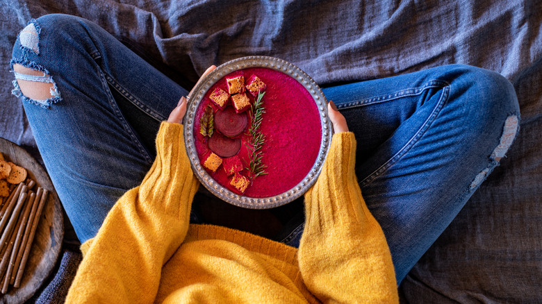 A person sitting cross-legged holding a bright pink bowl of beet soup