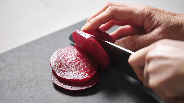 Hands slicing a red beet with a knife