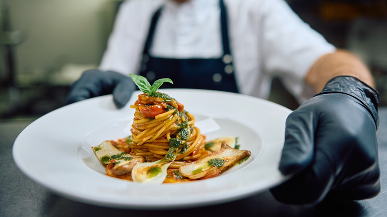 Chef putting plate of pasta in restaurant pass