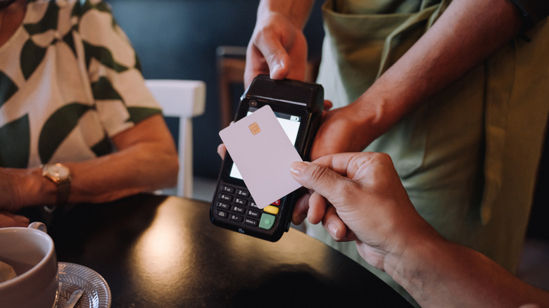 Hand tapping credit card on payment terminal at restaurant