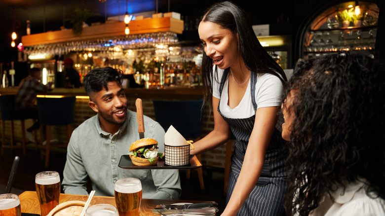 Restaurant server serving burger to customers drinking beer at casual restaurant