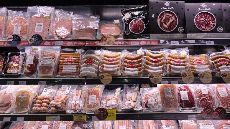 A variety of imported brand sausages and deli-style cold cuts including Salami, ham and smoked meats arranged in a refrigerated display shelf.