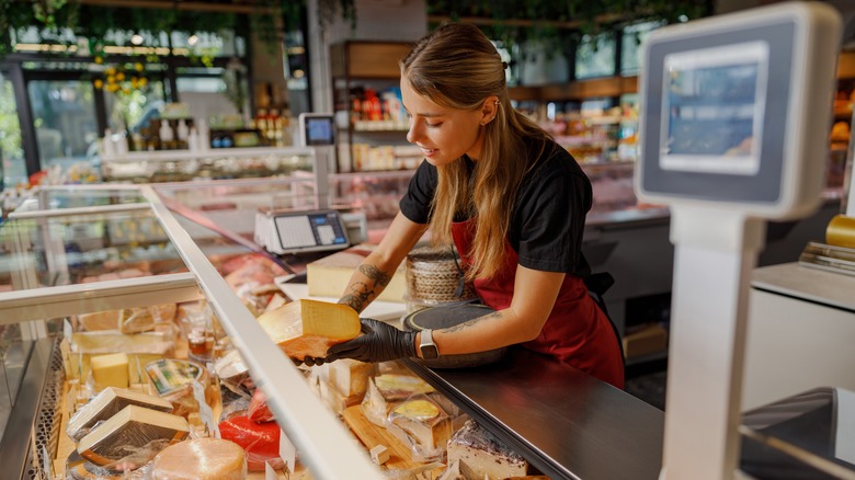 An employee slices a cheese at a deli shop.