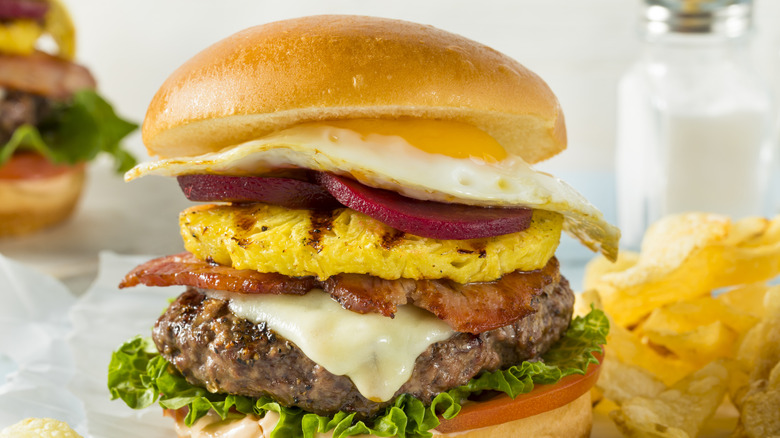 A classic Australian burger with the lot, including lettuce, tomato, patty, melted cheese, bacon, grilled pineapple, pickled beets, and a runny fried egg on a bun.
